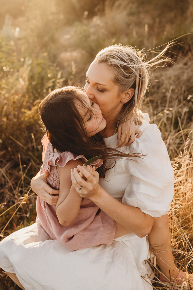 A mother embraces her daughter in a Melbourne field at sunset. The wind blows their hair.
