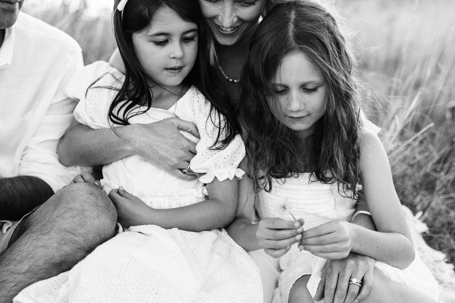 A black and white image of girls siting on their mother's lap, looking down at a flower.